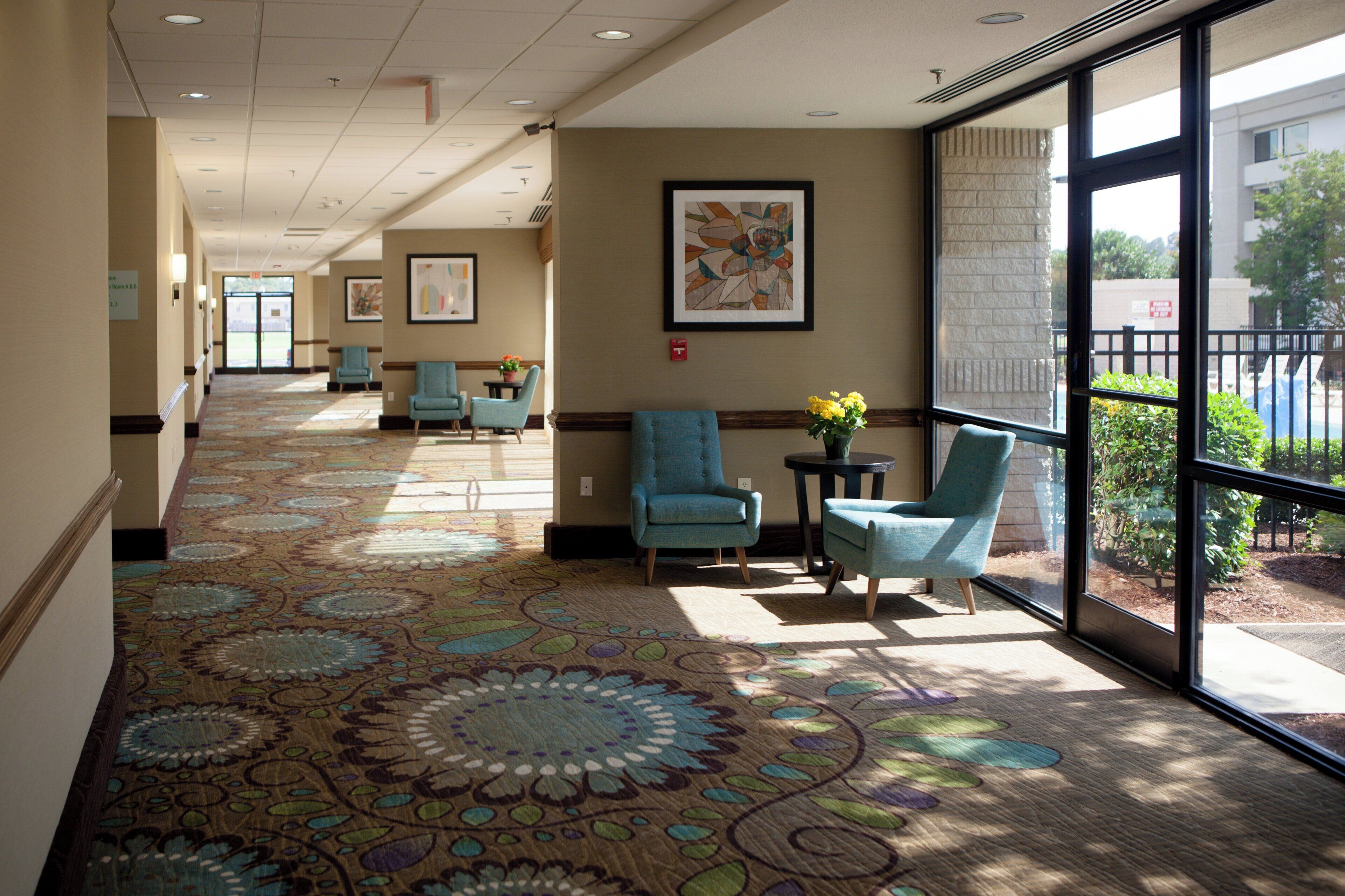 A hotel corridor with patterned carpet, seating areas, and artwork on the walls.