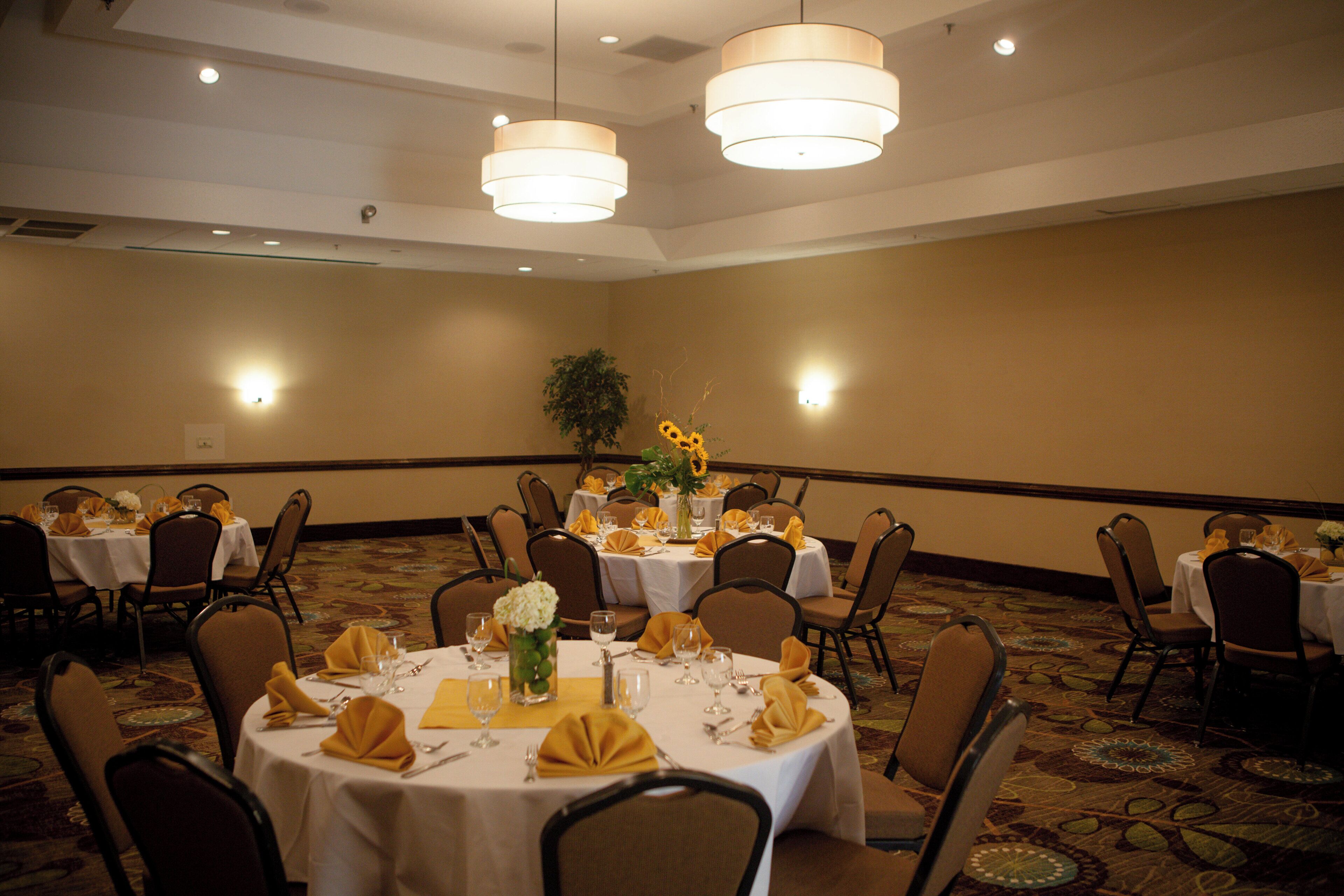 Un salón de conferencias con varias mesas dispuestas para comer, equipado con sillas e iluminación en el techo.