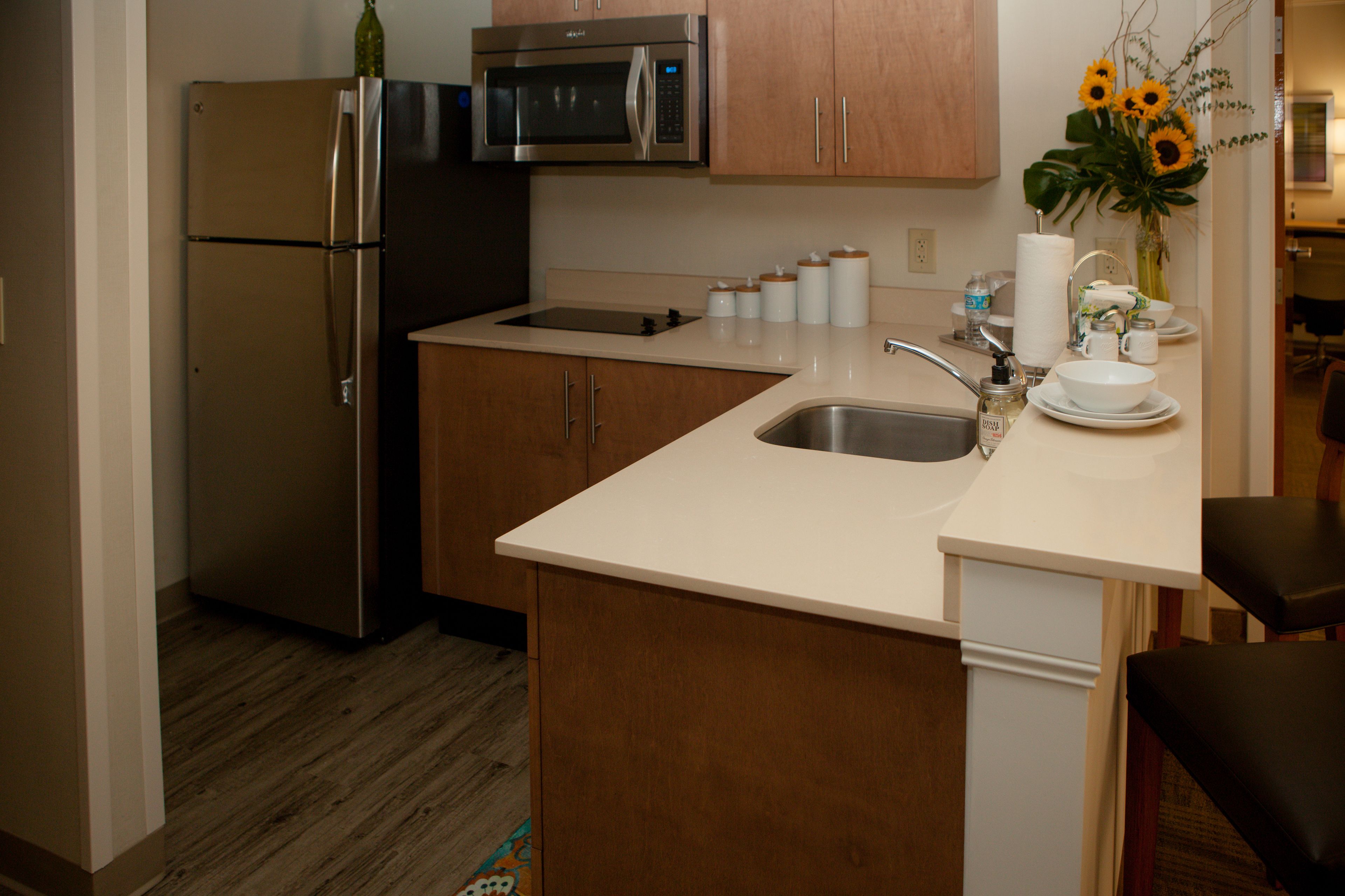 A kitchen with a refrigerator, microwave, sink, and wooden cabinets.