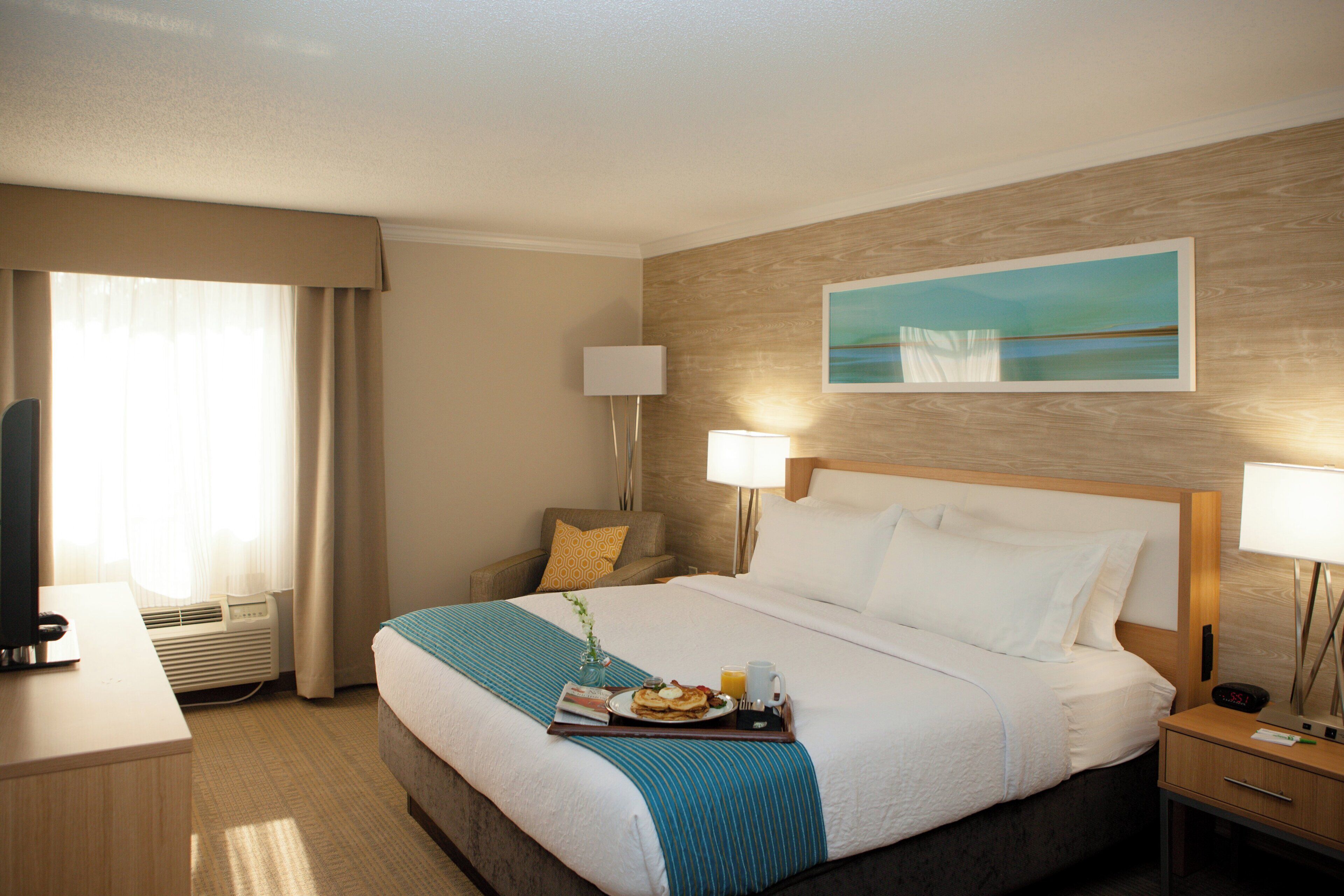 A hotel room with a bed, bedside tables, a desk, and a window with curtains.