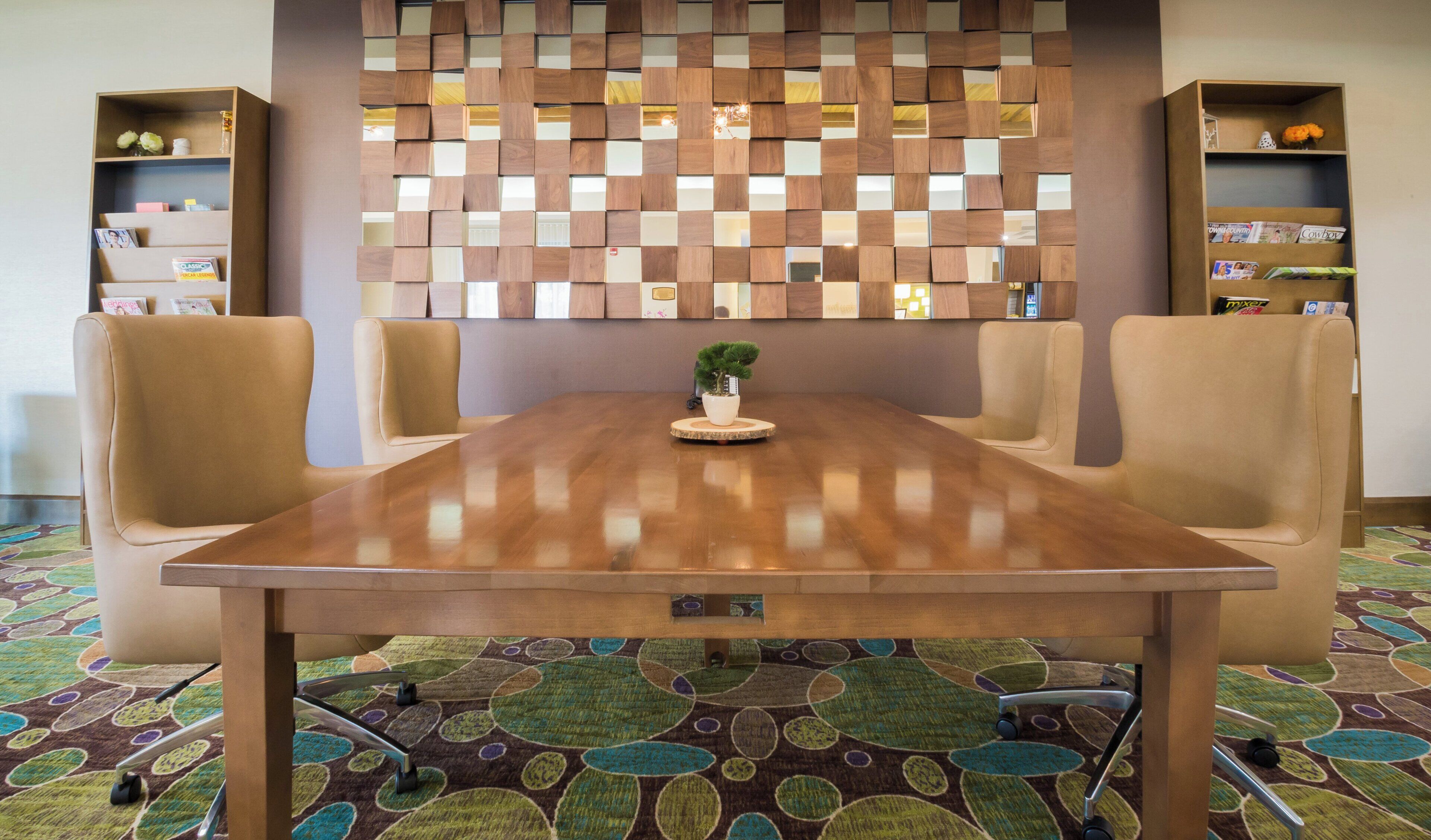 A conference room with a wooden table, four chairs, a potted plant, and a decorative wall panel.