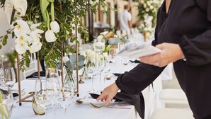 A table set with glassware, plates, and cutlery, and a person arranging the table settings. - Holiday Inn Greenville by IHG (Greenville)