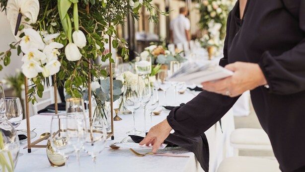 A table set with glassware, plates, and cutlery, and a person arranging the table settings. - Holiday Inn Greenville by IHG (Greenville)