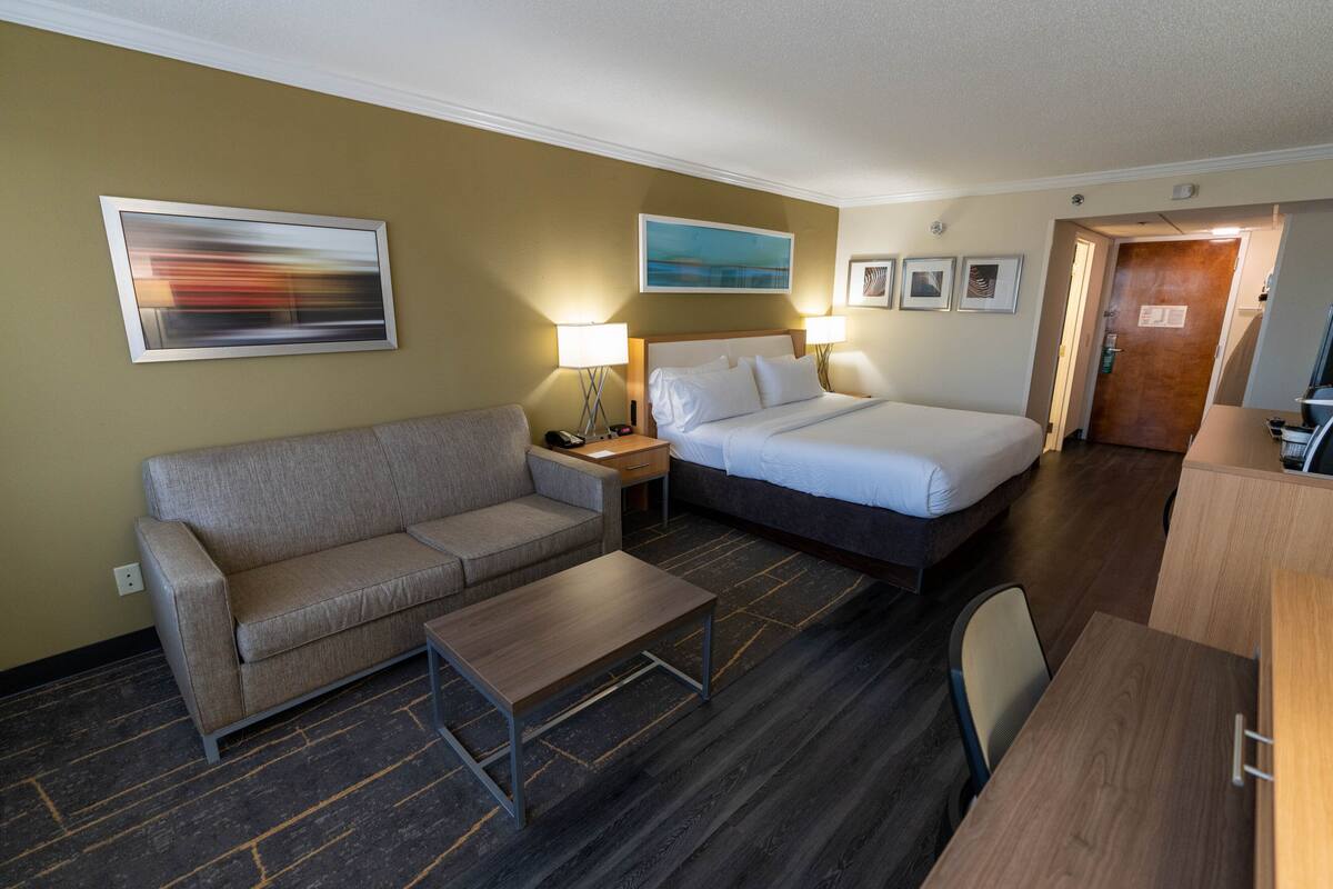 Ein Hotelzimmer mit Bett, Sofa, kleinem Tisch und Schreibtisch. An den Wänden befinden sich Wandleuchten und gerahmte Bilder.