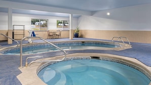 An indoor swimming pool with two lanes, a seating area with chairs, and a large window providing a view of the outside.