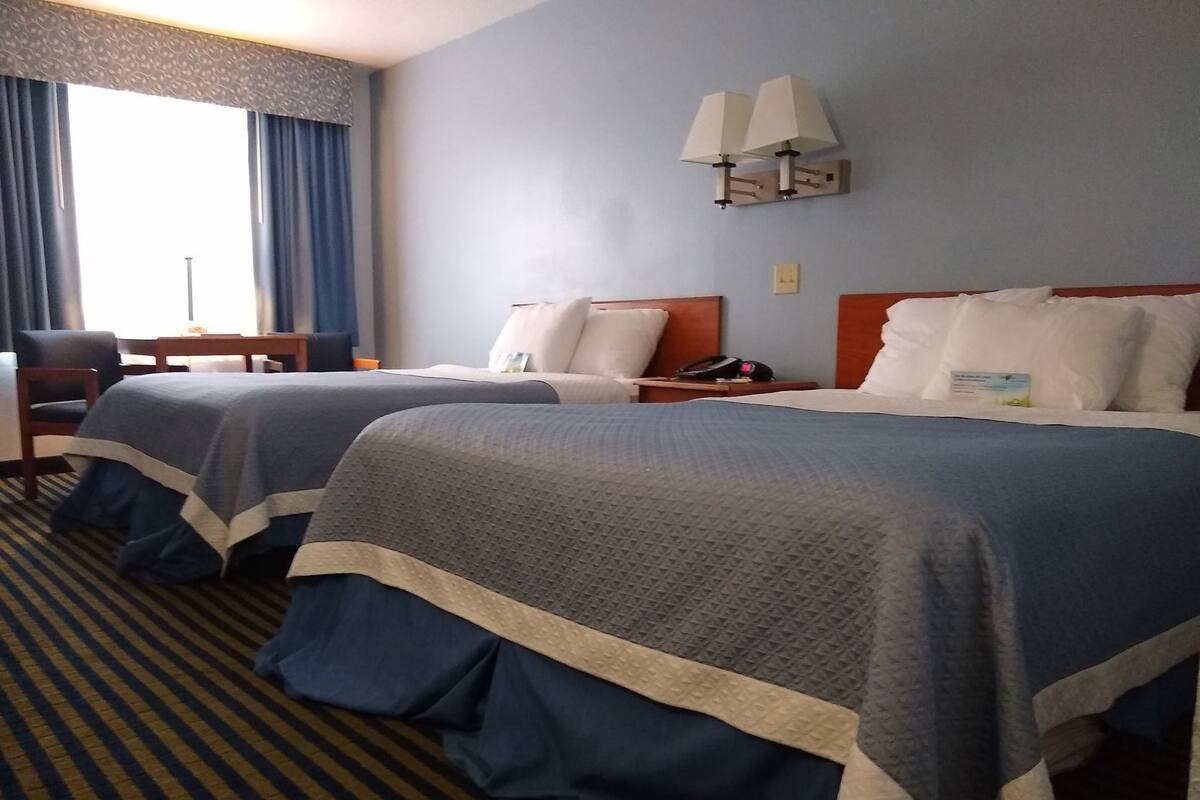 A hotel room with two beds, a desk, a chair, a lamp, and a window with curtains.