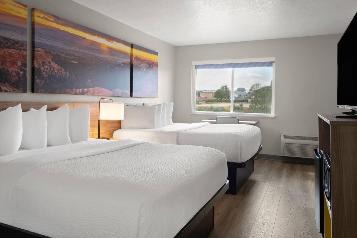 A hotel room with two beds, a large window with a view, and a painting on the wall.