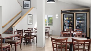 A dining area with wooden tables and chairs, a staircase, and a snack and cold beverage refrigerator.