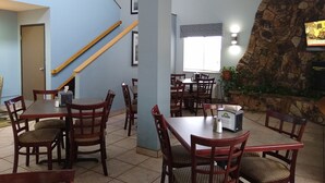 A restaurant with wooden tables and chairs, a stone accent wall, and a staircase.