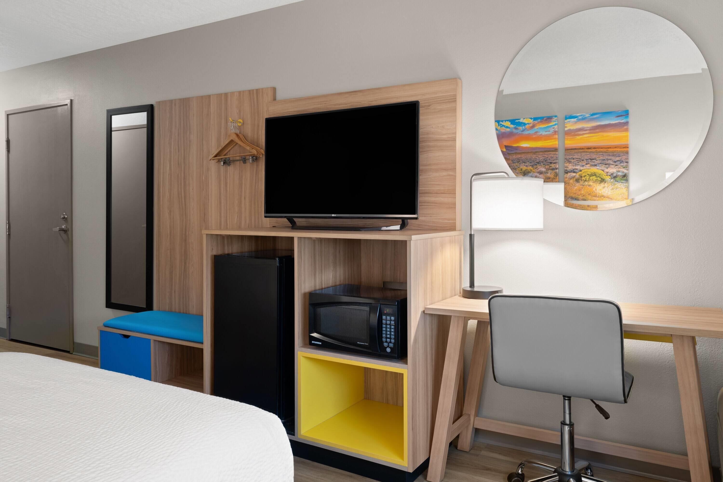 Habitación de hotel con cama, escritorio con silla, televisor, microondas, armario y espejo.
