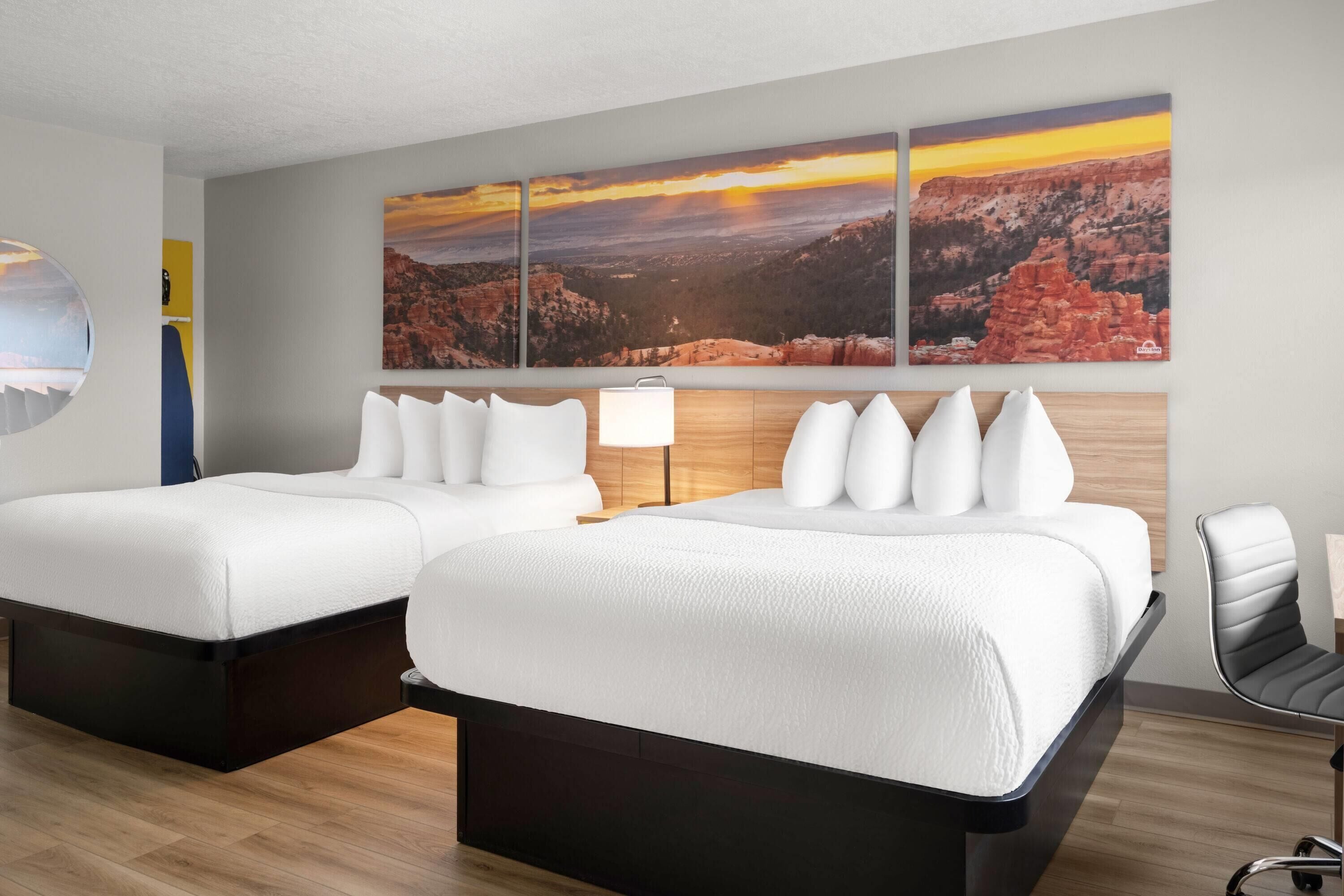 Ett hotellrum med två sängar, en sänggavel i trä, en stor landskapsmålning och en modern stol.
