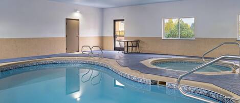 An indoor swimming pool with two separate sections, a door, a window, and a table with chairs.