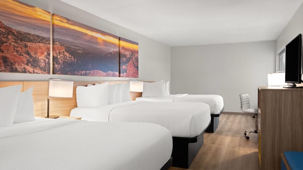 A hotel room with three beds, a desk with a computer, and a large painting of a canyon. - Days Inn by Wyndham Las Vegas (Las Vegas)