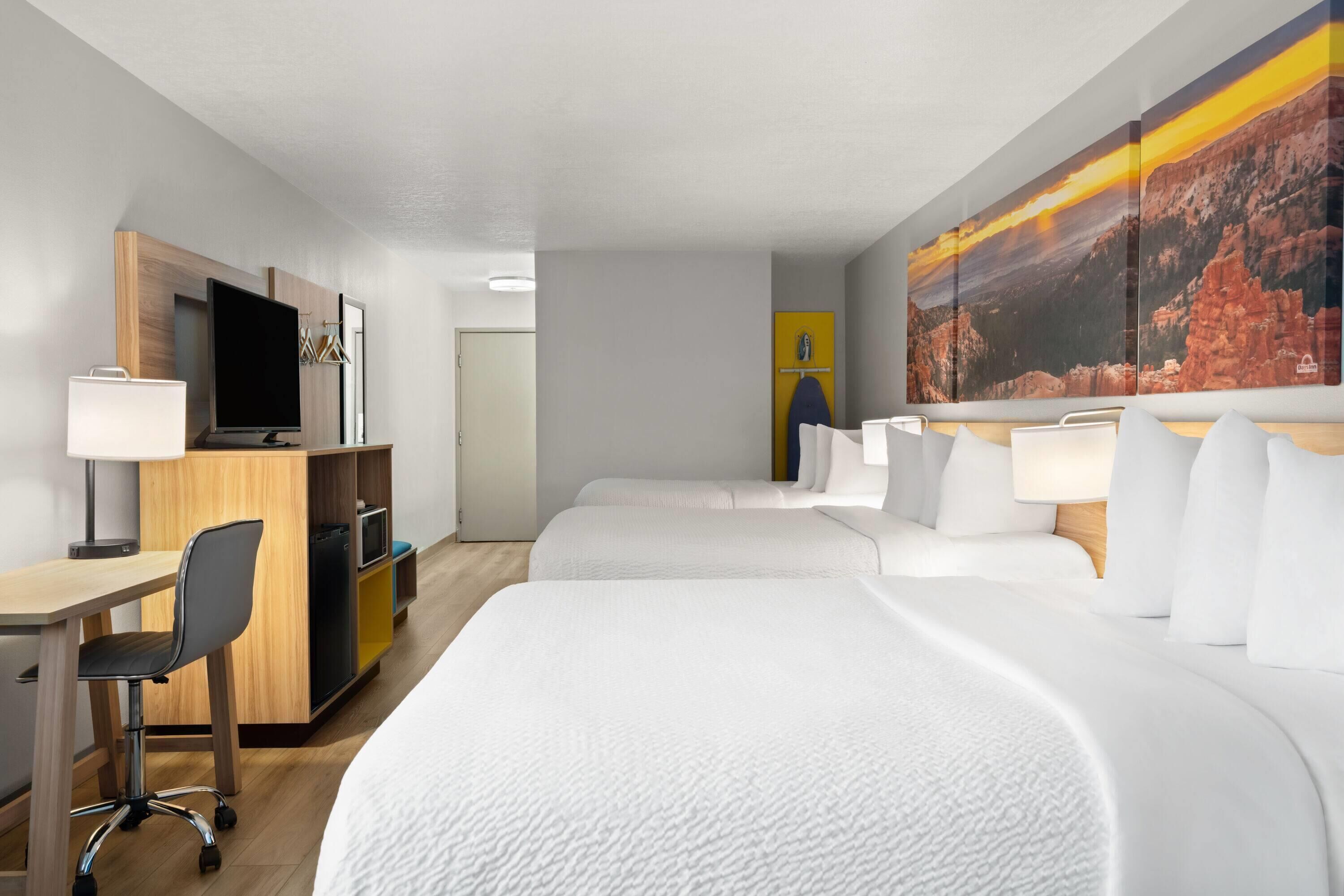 Een hotelkamer met twee bedden, een bureau, een stoel, een televisie en een groot schilderij aan de muur.
