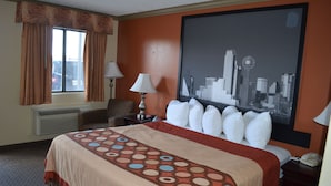 A hotel room with a bed, a cityscape painting, a lamp, and a window with curtains. - Hill Country Inn & Suites (Copperas Cove)