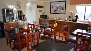 A dining area with wooden chairs and tables, a refrigerator, a microwave, and a coffee machine. - Hill Country Inn & Suites (Copperas Cove)
