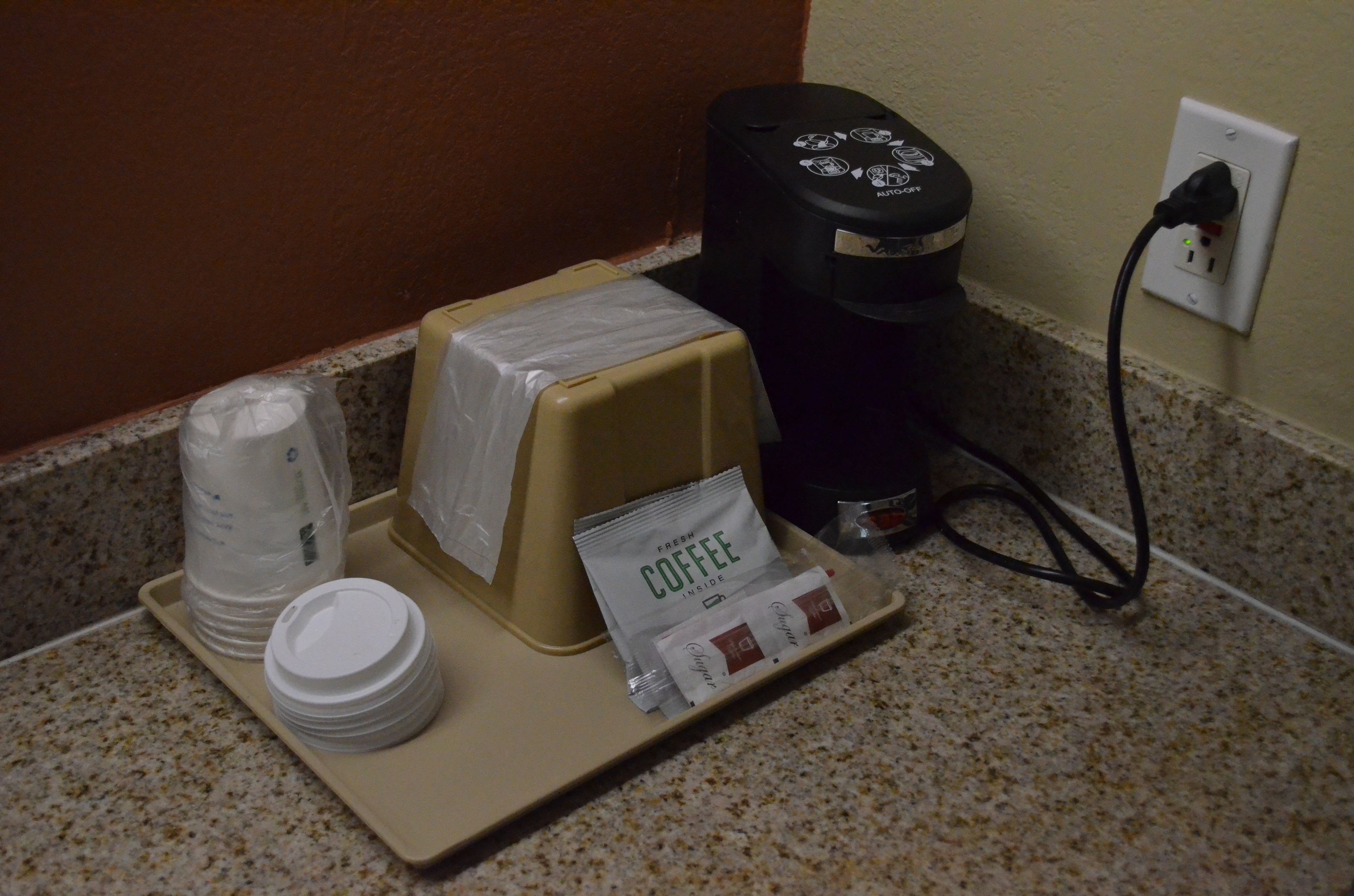 A coffee station with a coffee maker, disposable cups, and a coffee bag on a tray.