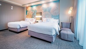 A hotel room with two beds, a desk, a chair, and a lamp.