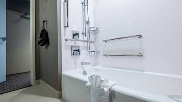 A modern bathroom with a white bathtub, grab bars, a towel rack, and a shower area.