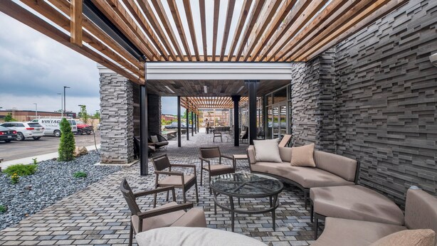 An outdoor patio area with a wooden pergola, stone wall, and seating arrangements including sofas and chairs.