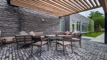 An outdoor patio with a stone wall, wooden pergola, and outdoor furniture.