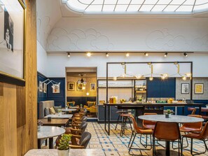 Un restaurante con techo alto, suelo estampado y varias zonas de estar, incluyendo mesas y cabinas.