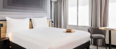 A modern hotel room with a large bed, a desk, a chair, and a view of the outdoors.