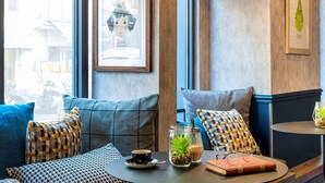 A cozy seating area with a table, a framed picture, and a window with a view of buildings. - Ibis Paris Grands Boulevards Opera 9th (Paris)