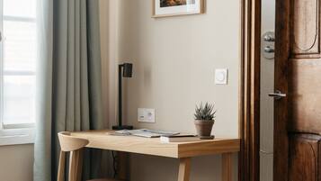 Een kamer met een houten bureau, een stoel, een kamerplant, een lijst met een afbeelding aan de muur en een houten deur.