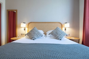A hotel room with a large bed, two bedside lamps, a wooden headboard, and a patterned bedspread.
