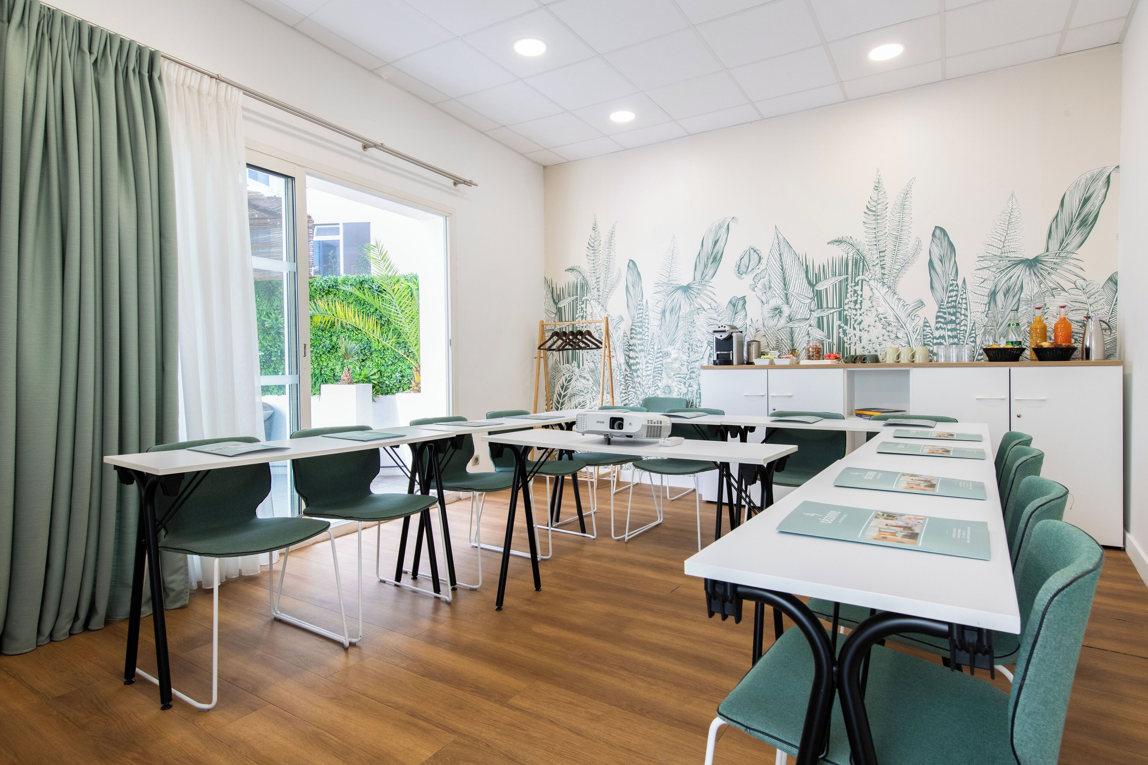 A conference room with tables, chairs, a projector, and a plant wall.