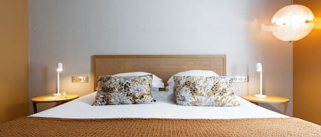 Una cama bien hecha con almohadones estampados, una manta marrón con textura y dos mesitas de noche con lámparas.