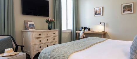 A hotel room with a large bed, a TV mounted on the wall, a desk with a lamp, a dresser, and a chair.