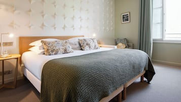 Una cama bien tendida con una manta verde, una mesita de noche con una lámpara y una pared con un diseño geométrico.