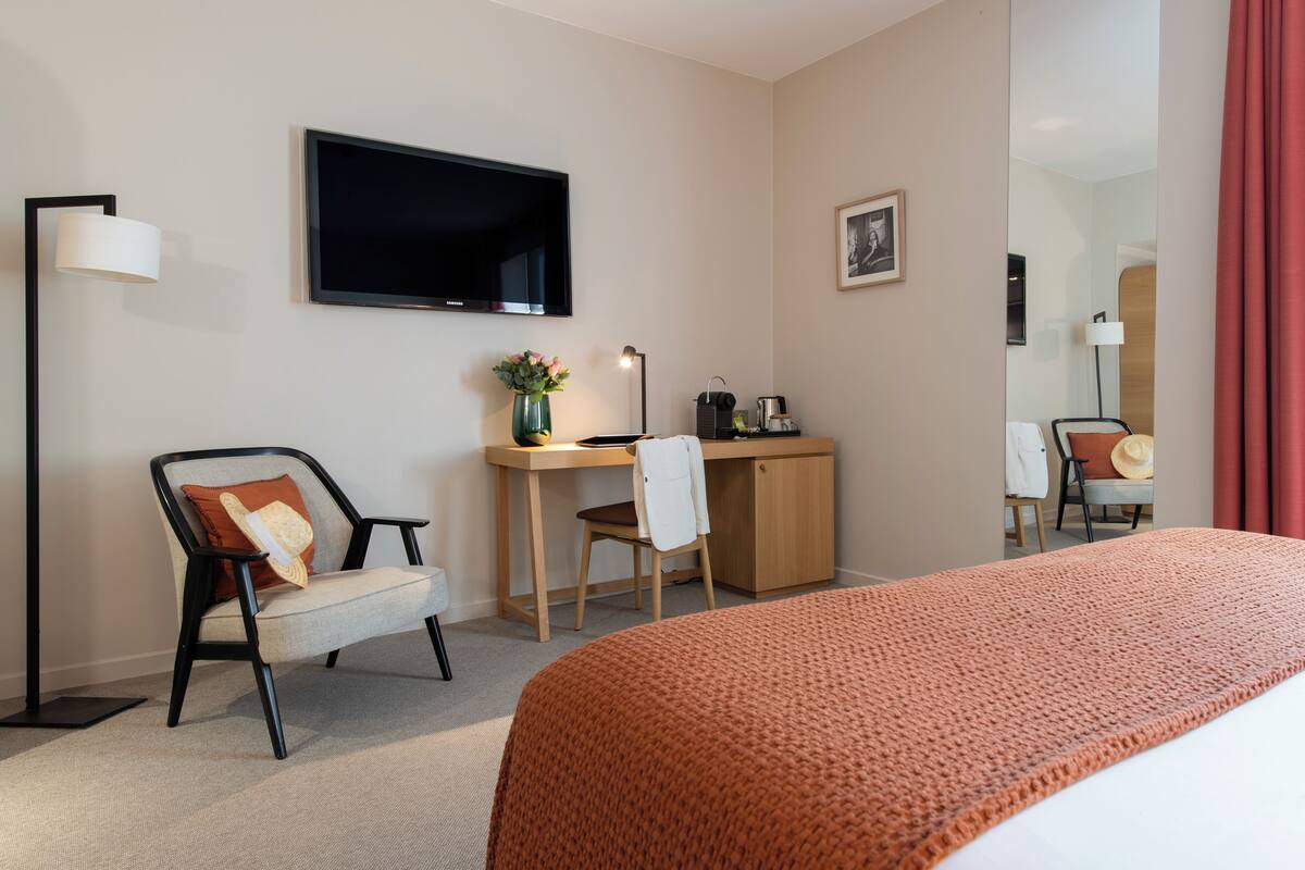 Une chambre d’hôtel équipée d’un lit, d’un bureau, d’une chaise, d’une télévision et d’un miroir.