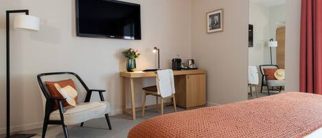 Habitación de hotel con cama, escritorio, silla, televisor y espejo.
