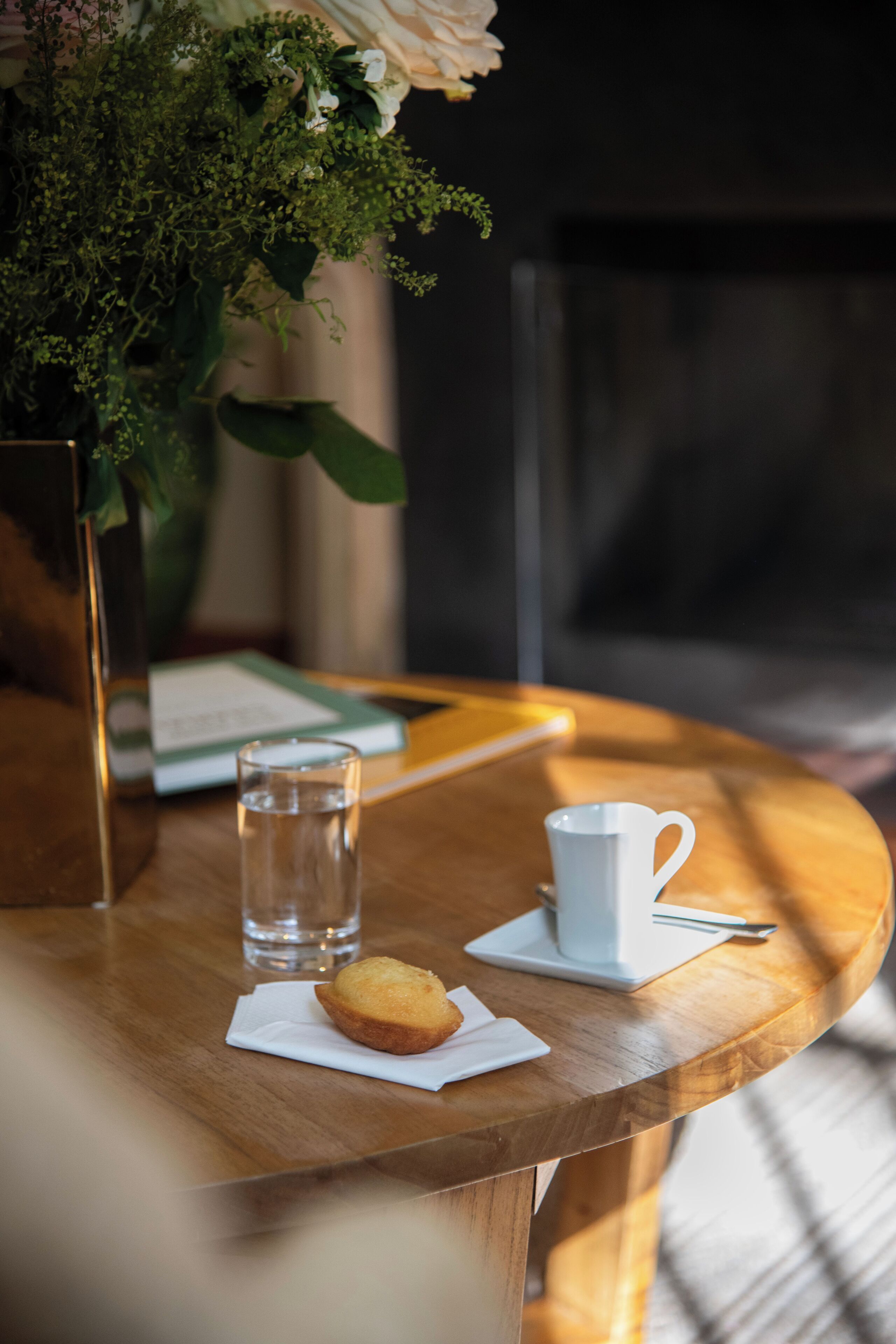 A round wooden table with a muffin, a glass of water, and a white cup.