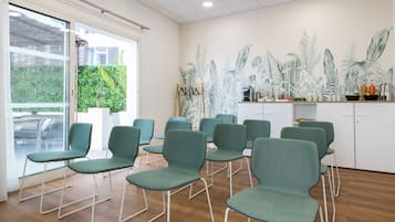 A room with green chairs arranged in a semi-circle, a white cabinet with various items, and a wall mural of tropical plants.