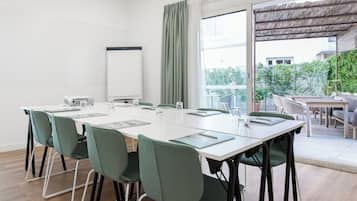 Un salón de conferencias con una mesa larga, sillas verdes, una pizarra y vistas a un balcón con mobiliario exterior.