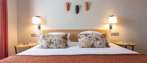 A hotel room with a large bed, two bedside tables, a nightstand, and two wall-mounted lamps.