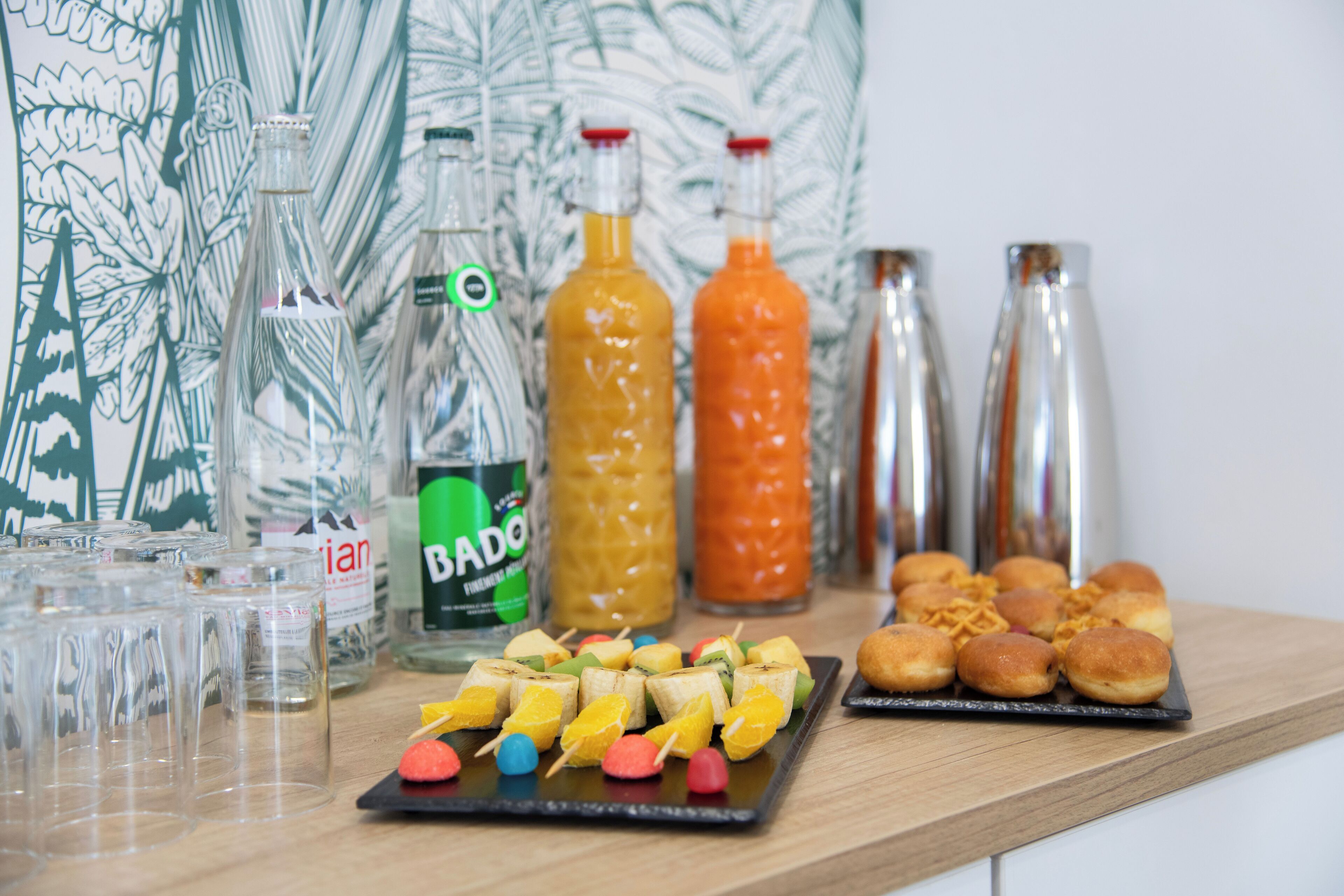 A table with various food items, including fruit skewers and pastries, and several bottles of beverages.