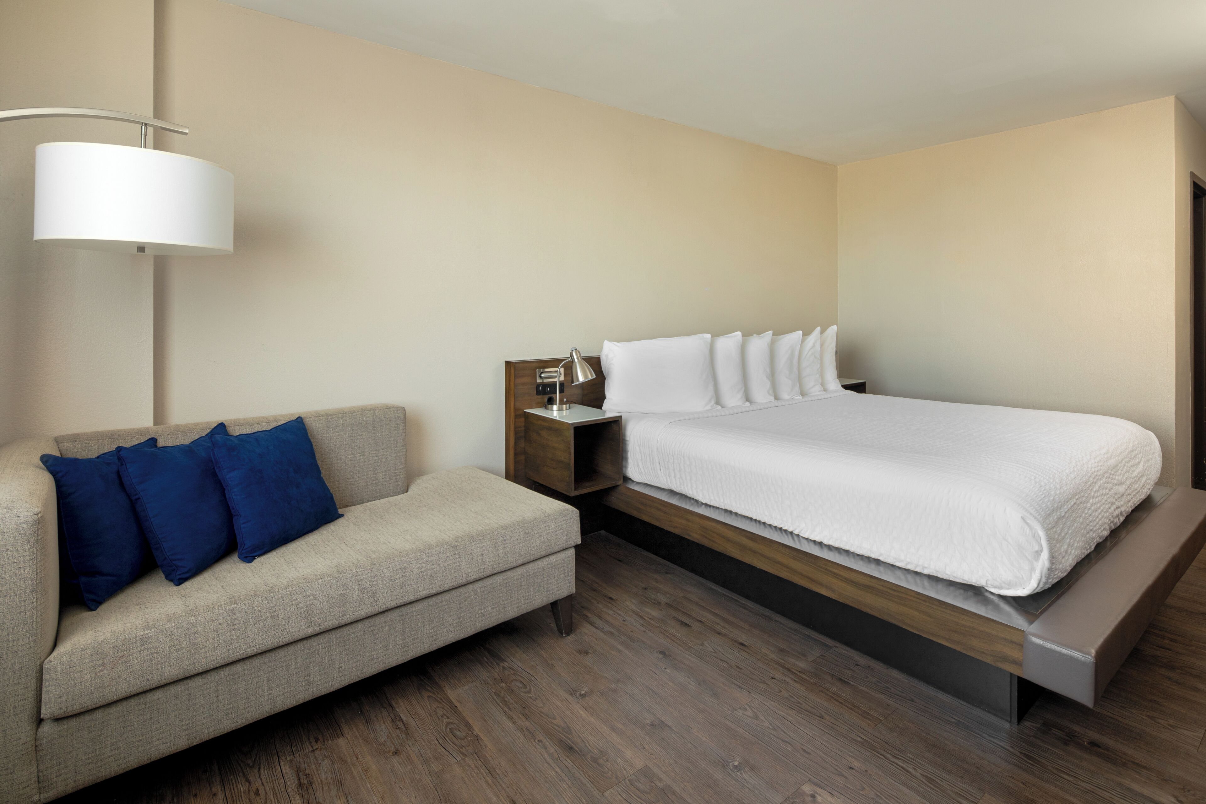 A modern hotel room with a bed, a sofa, a nightstand, and a lamp.