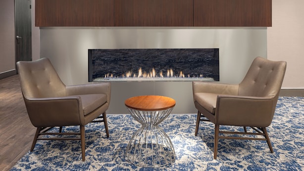 A modern interior with a fireplace, two leather chairs, a round table, and a patterned rug. - The Lodge at Duke Medical Center (Durham)