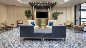 A modern lobby with a sofa set, two armchairs, a coffee table, and a TV screen. - The Lodge at Duke Medical Center (Durham)