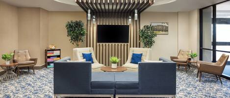 A modern lobby with a sofa set, two armchairs, a coffee table, and a TV screen.