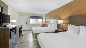 Habitación de hotel con dos camas, un escritorio, televisor, lámpara y ventana con persianas.