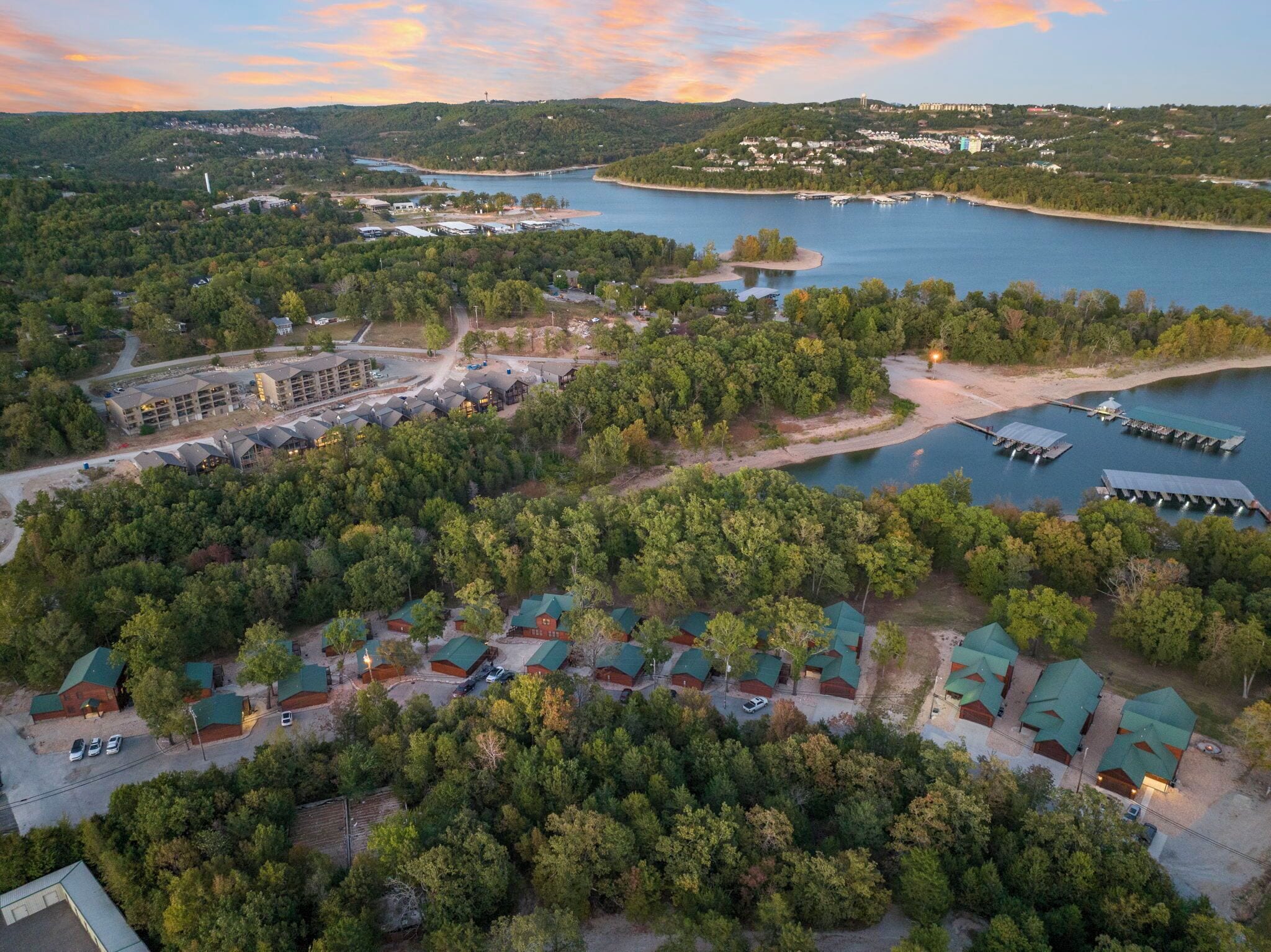 An aerial view of a lakeside resort with multiple cabins, a large building complex, and docked boats.