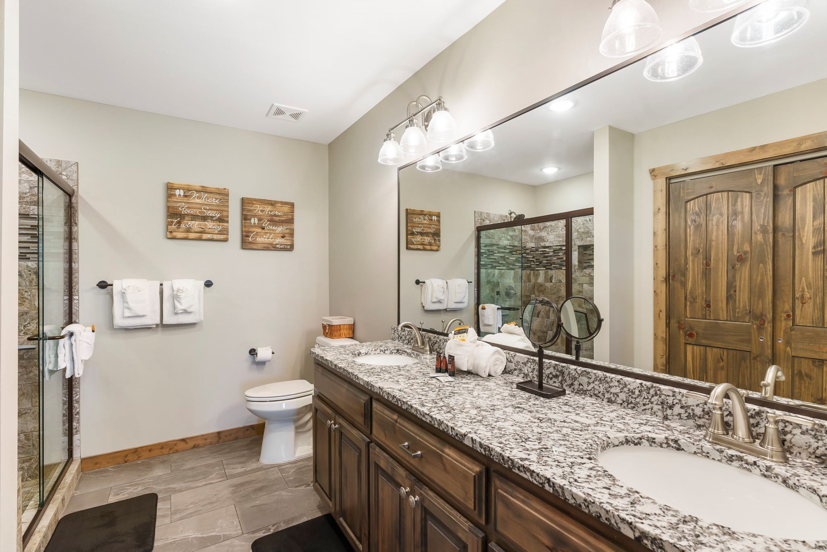 A bathroom with a granite countertop, two sinks, a large mirror, and wooden cabinets.