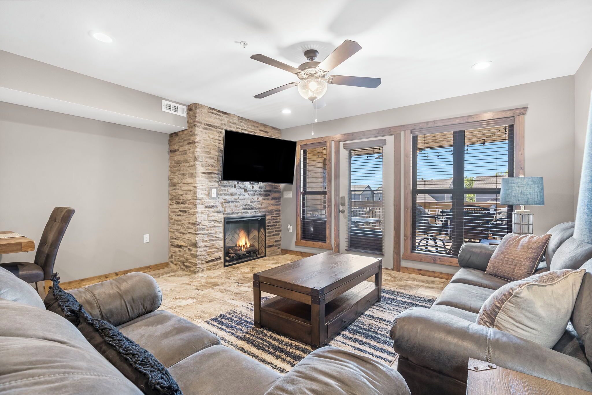 A living room with a stone fireplace, leather sofas, a coffee table, and a ceiling fan.