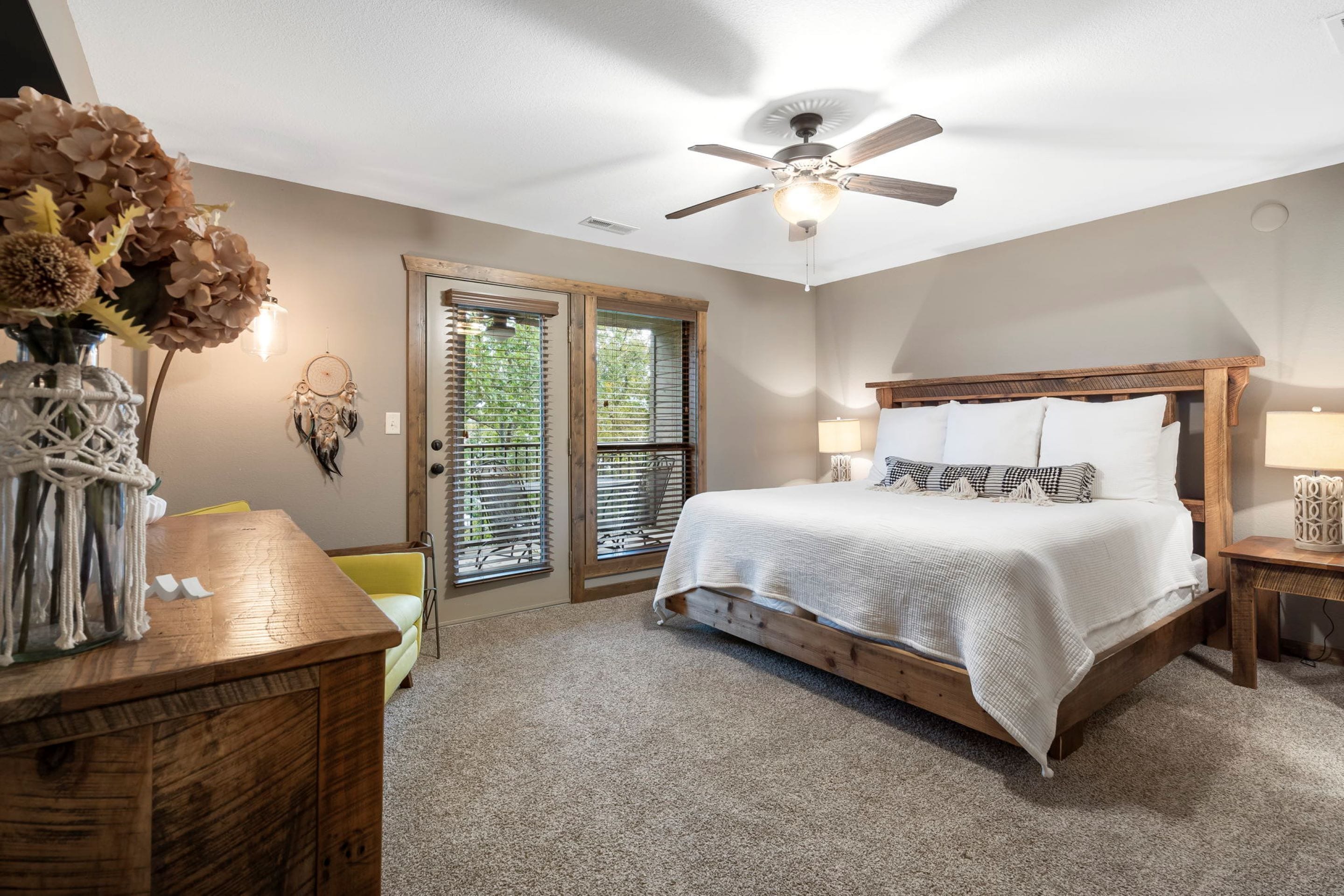 A bedroom with a bed, wooden headboard, bedside tables, a ceiling fan, and a door with glass panels.